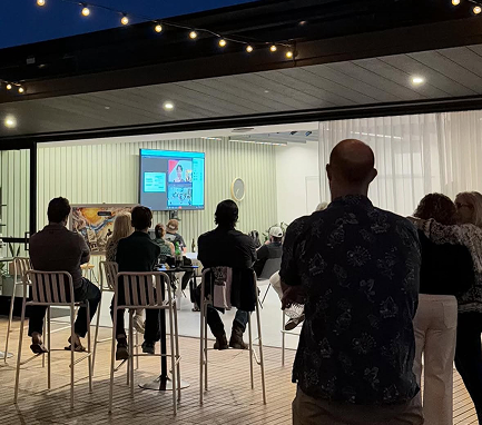 Attendees seated on a string-lit patio at dusk watching a presentation at a Heterodox Research Society event